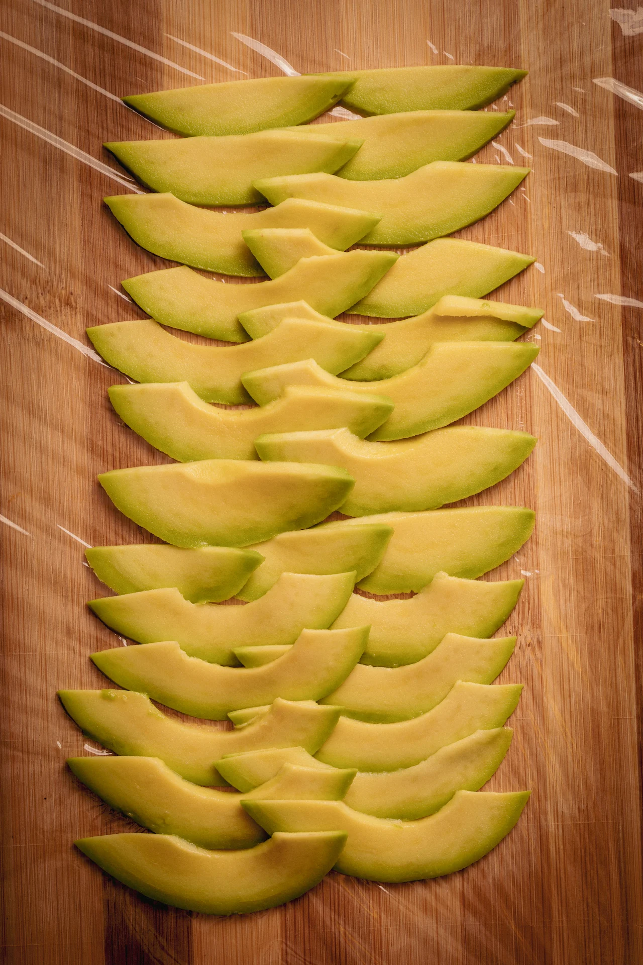 Fotografía gastronómica de láminas de aguacate organizadas en abanico sobre tabla de madera con film — Jose Fonseca Medellín