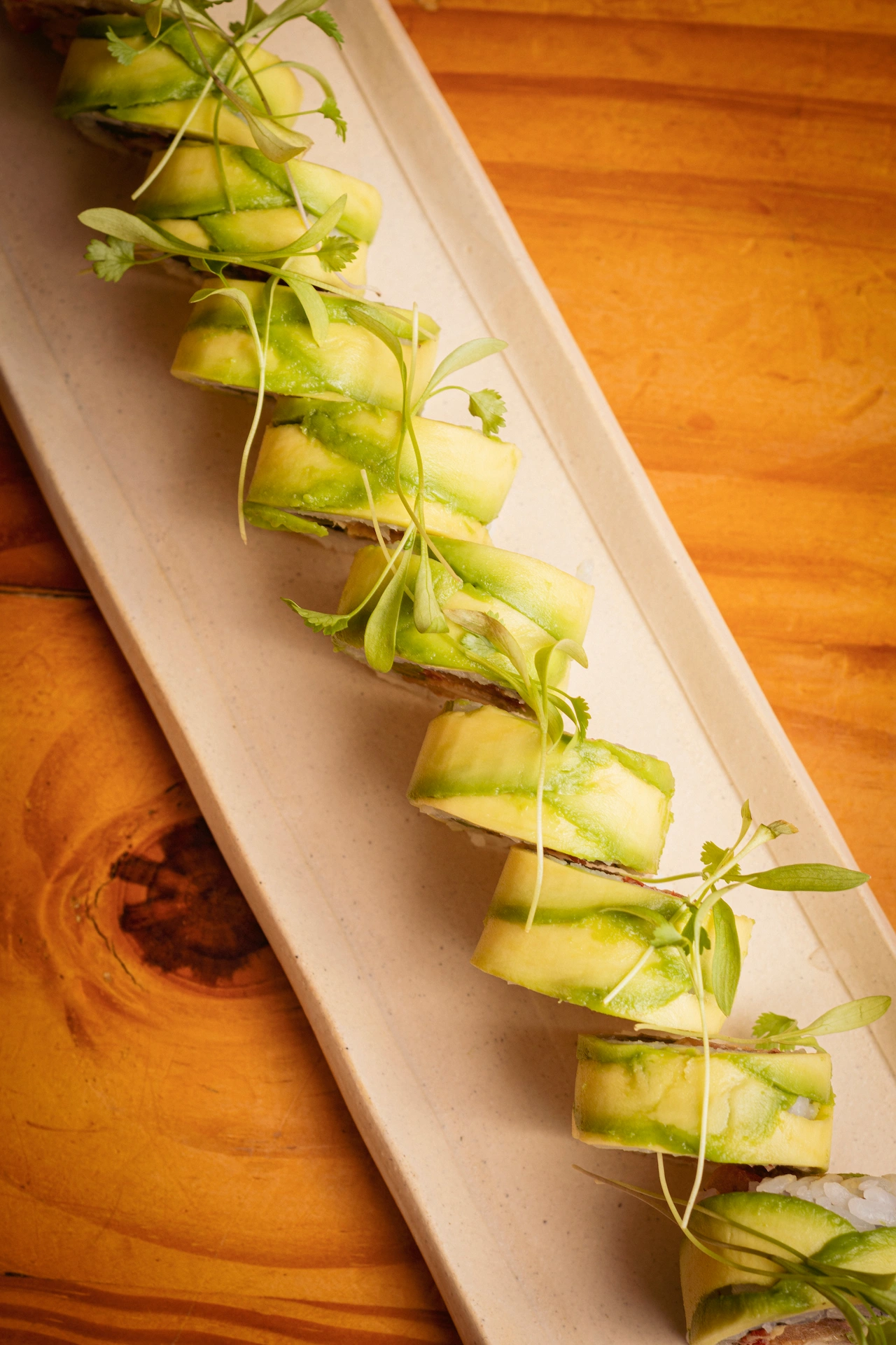 Fotografía gastronómica de roll de sushi cubierto de láminas de aguacate y microgreens en bandeja rectangular — Jose Fonseca Medellín
