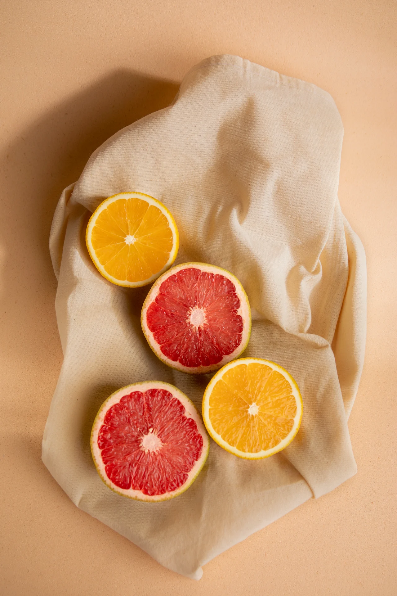 Fotografía gastronómica de cuatro mitades de toronja y naranja sobre tela de lino crudo en fondo durazno — Jose Fonseca Medellín