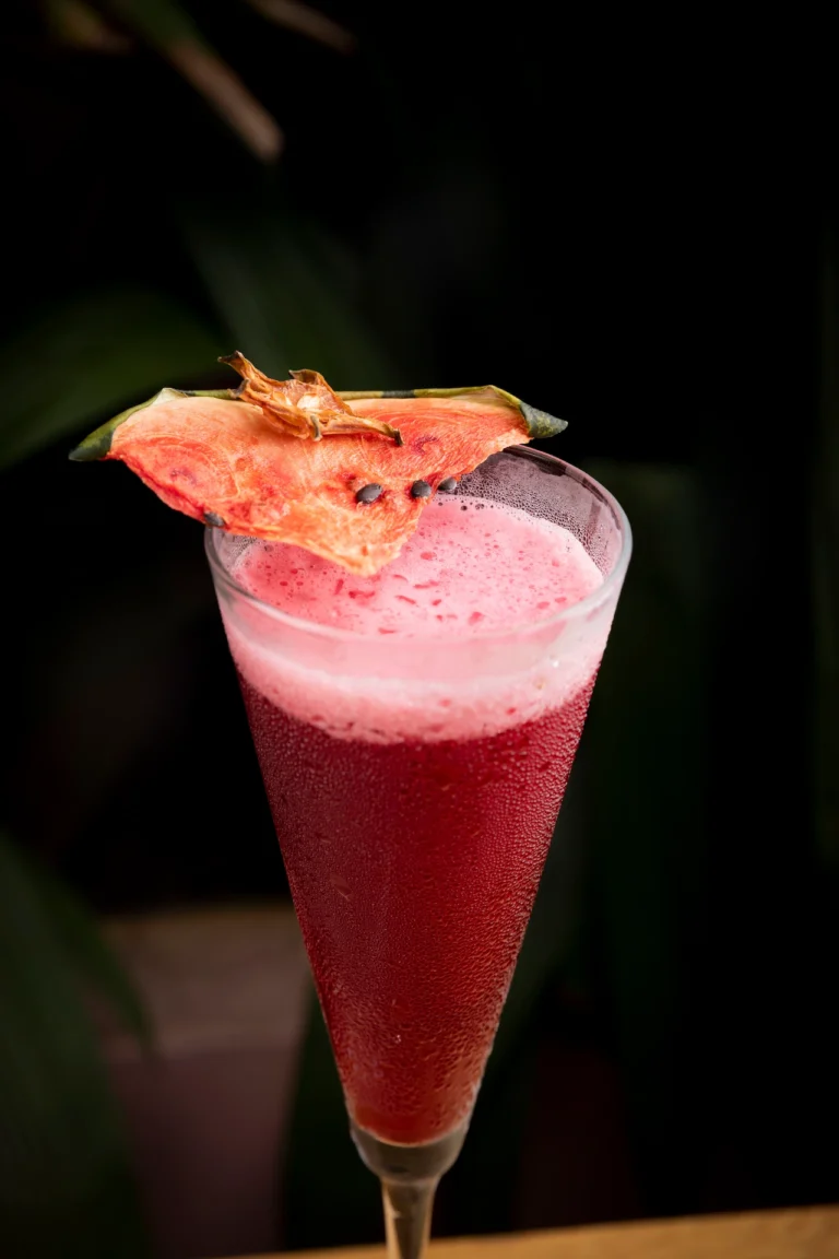 Fotografía gastronómica de cóctel rojo con chip de sandía deshidratada en copa flauta, fondo oscuro — Jose Fonseca Medellín