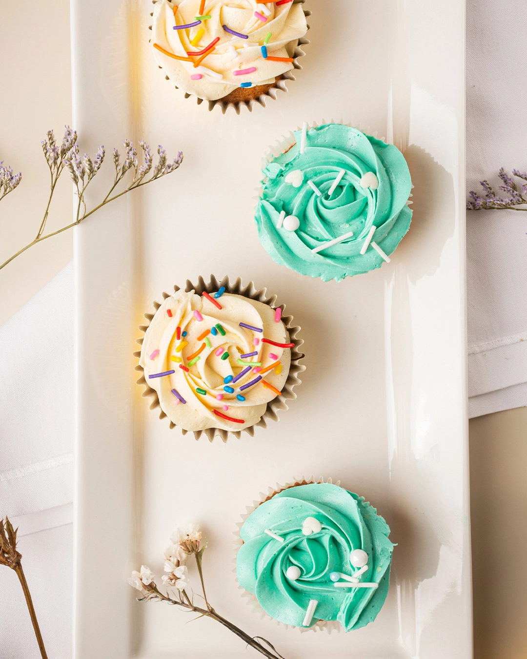 Fotografía gastronómica de cupcakes con frosting azul turquesa y vainilla en fuente blanca con flores decorativas — Jose Fonseca Medellín