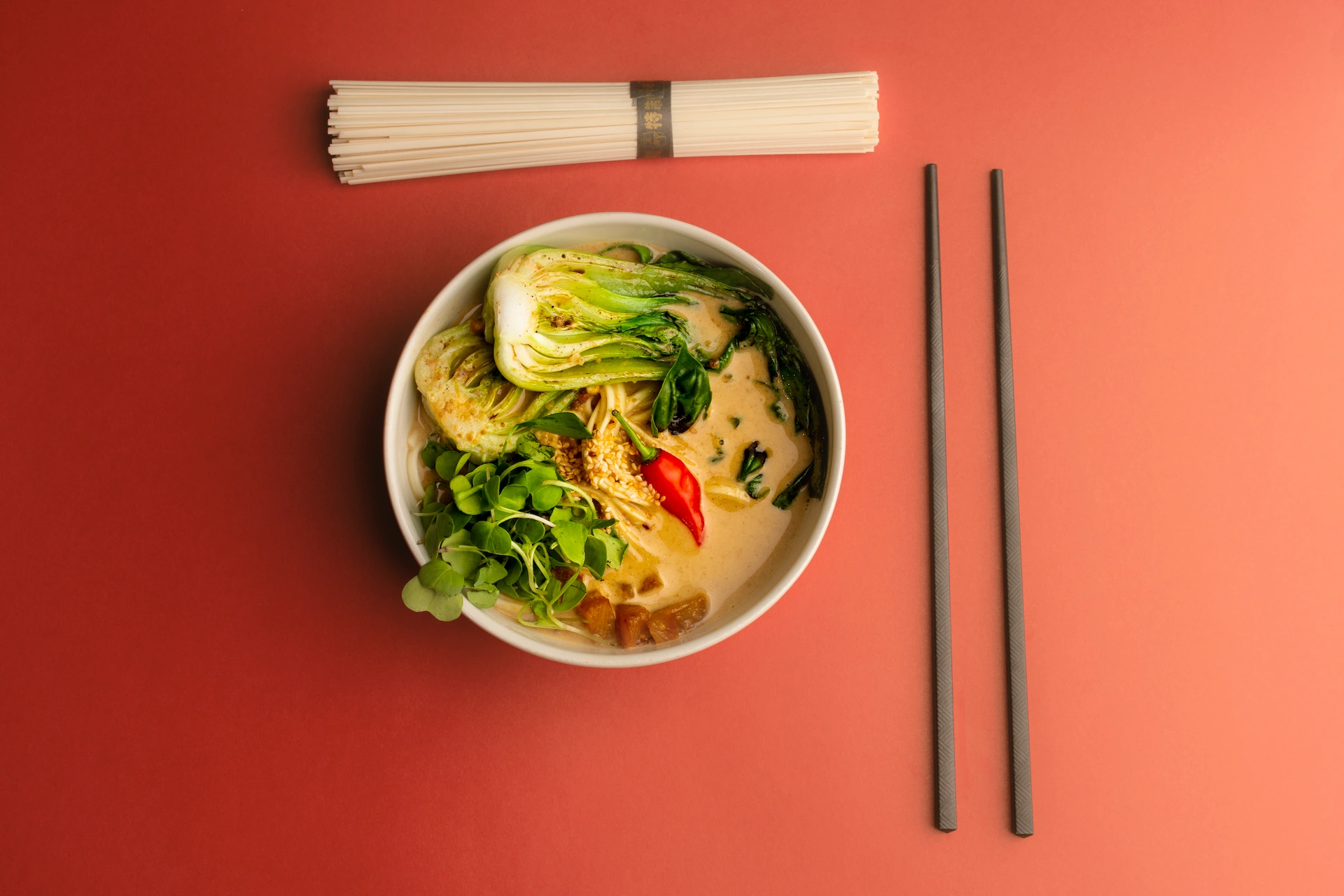 Fotografía gastronómica cenital de ramen vegano con curry de maní, bok choy, tofu y ají en fondo rojo — Jose Fonseca Medellín