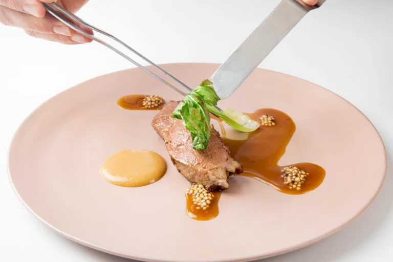 Fotografía gastronómica de chef emplatando corte de pato con jus y verduras en plato rosado de alta cocina — Medellín