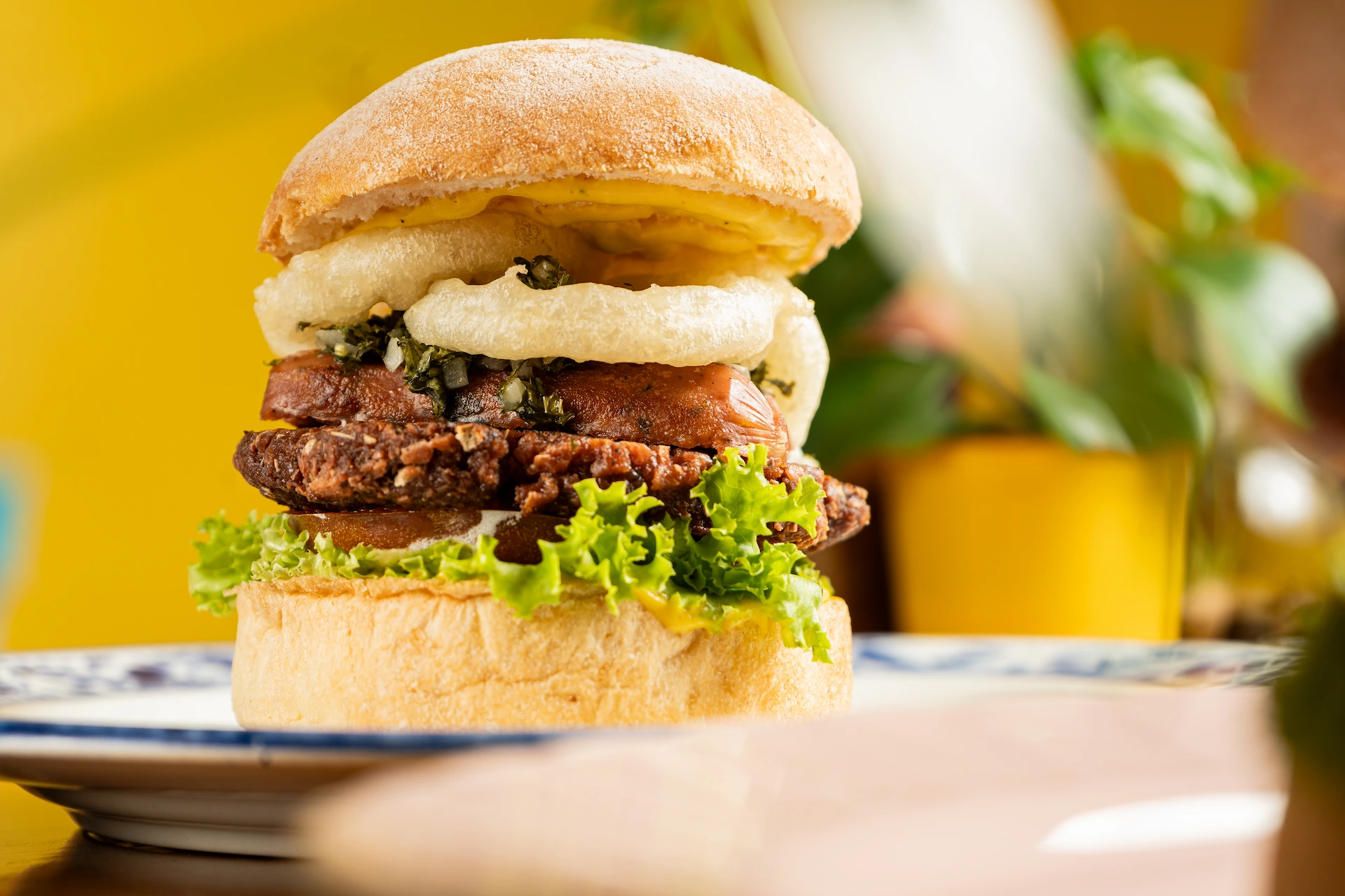 Fotografía gastronómica de hamburguesa plant based doble con champiñón, cebolla y tomate en fondo amarillo — Jose Fonseca Medellín