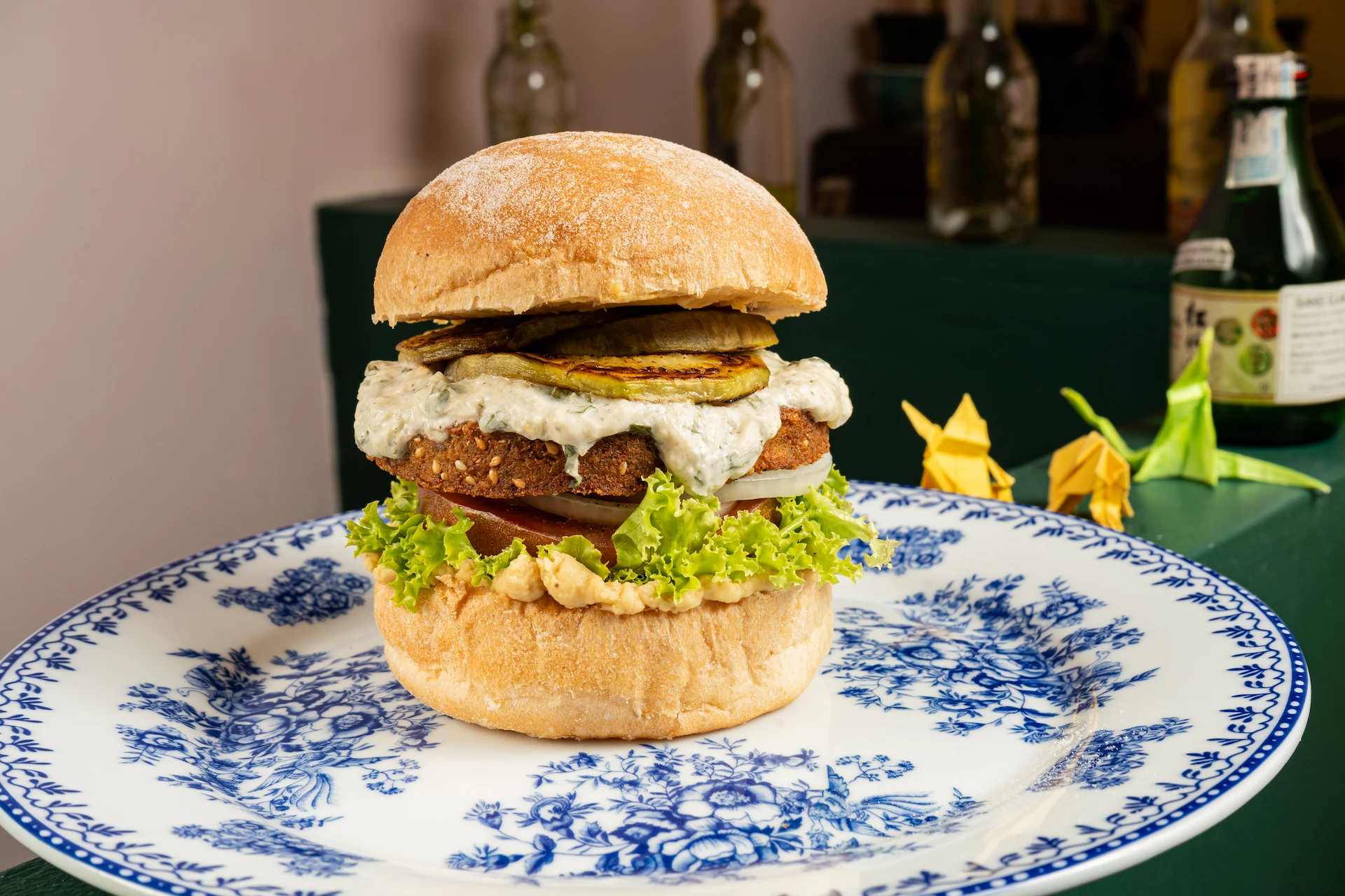Fotografía gastronómica de hamburguesa vegana con paty de falafel, pepino grillado y salsa tzatziki en plato porcelana azul — Jose Fonseca Medellín