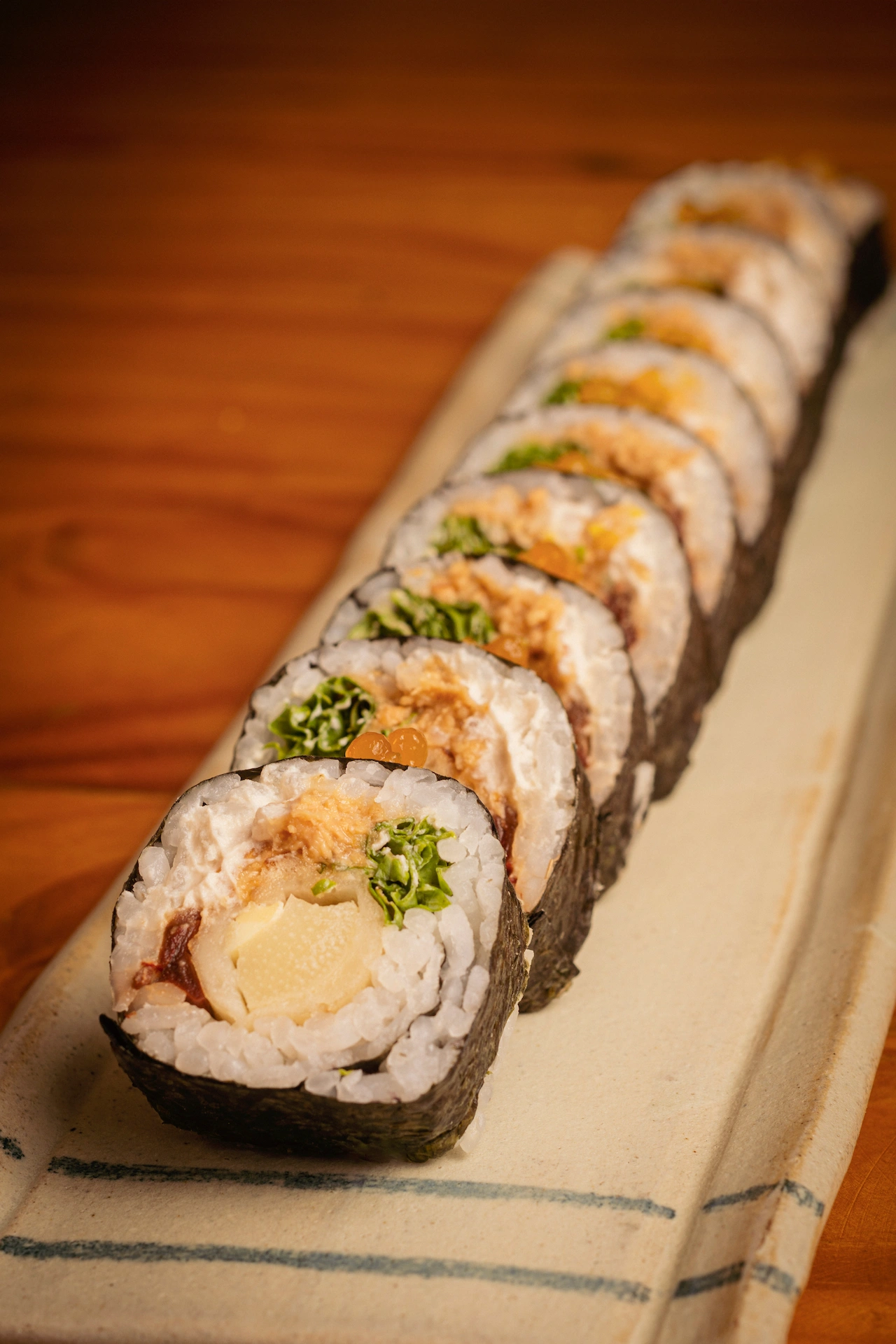 Fotografía gastronómica lateral de maki vegano con relleno de vegetales y esferas naranjas sobre bandeja con lino — Jose Fonseca Medellín