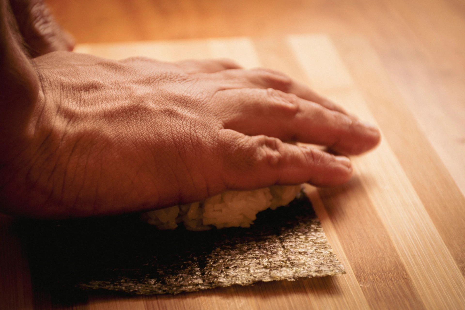 Fotografía gastronómica de manos armando roll de sushi sobre hoja de nori en tabla de madera — Jose Fonseca Medellín