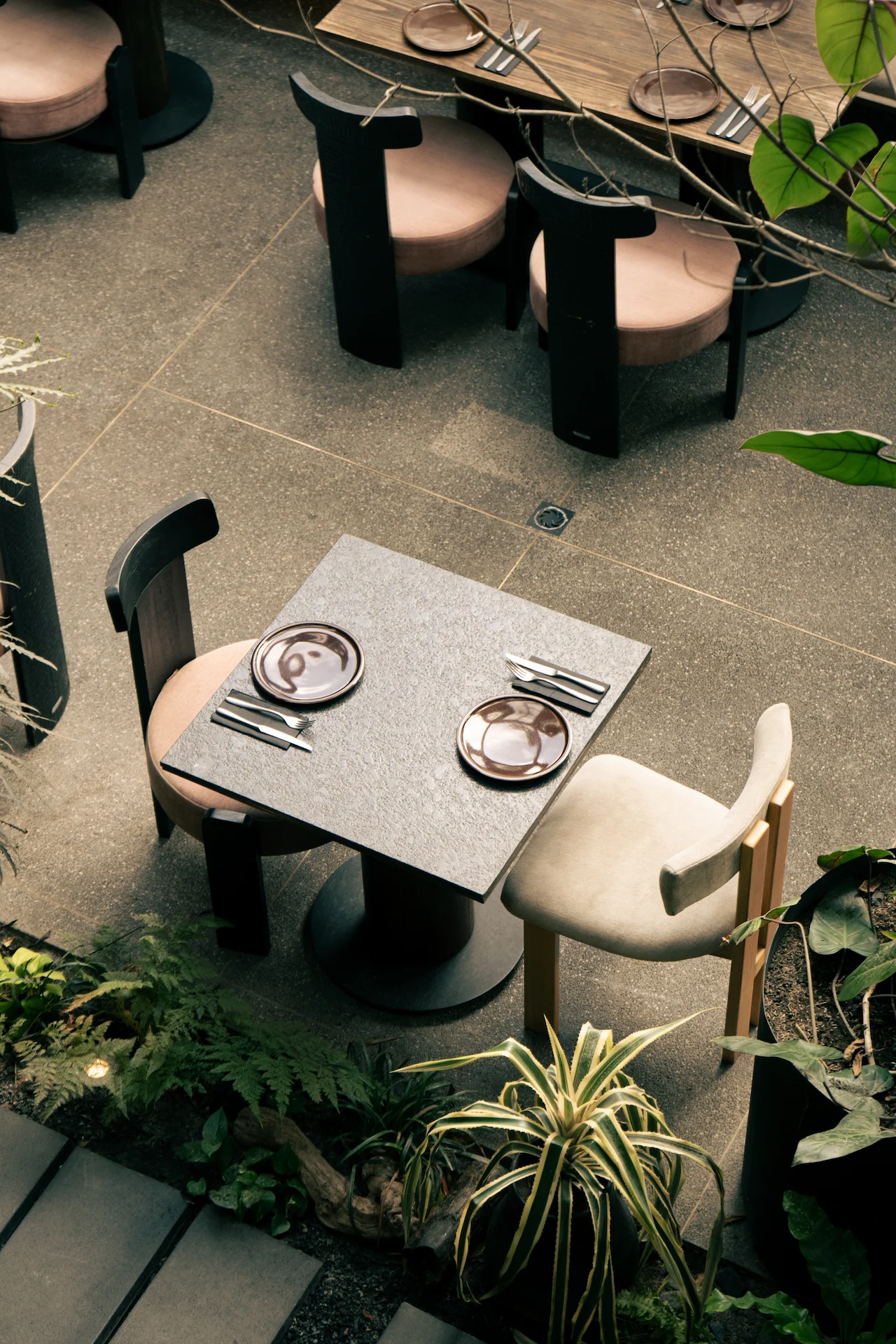 Fotografía gastronómica cenital de mesas de piedra con sillas de diseño y platos de cerámica rosa en jardín tropical — Jose Fonseca Medellín