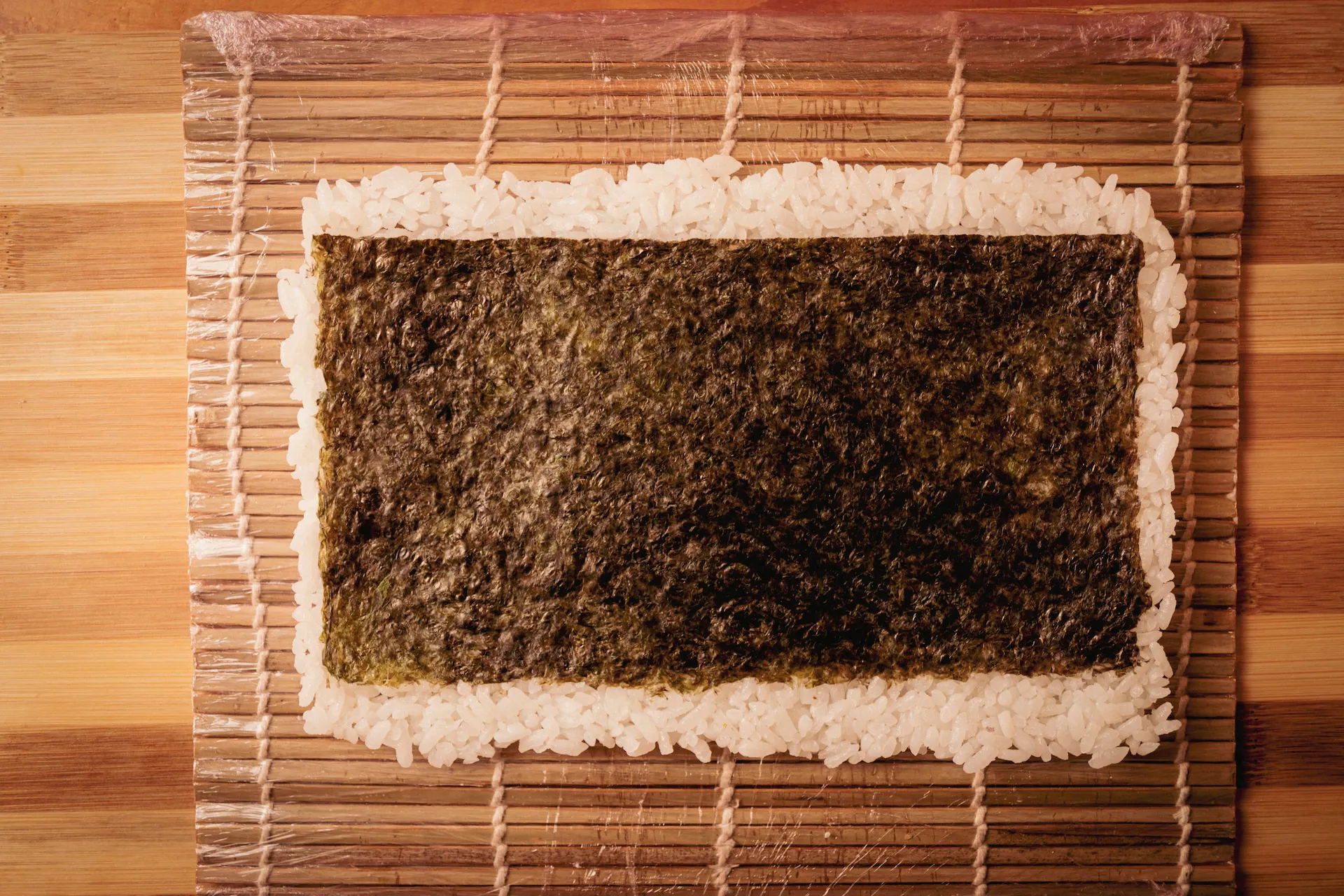 Fotografía gastronómica cenital de hoja de nori con capa de arroz sobre esterilla de bambú, preparación ura maki — Jose Fonseca Medellín