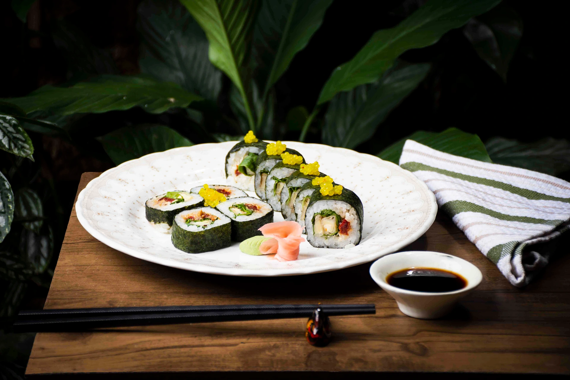 Fotografía gastronómica de sushi vegano con huevas en plato blanco, palillos y salsa soya, fondo de plantas — Jose Fonseca Medellín