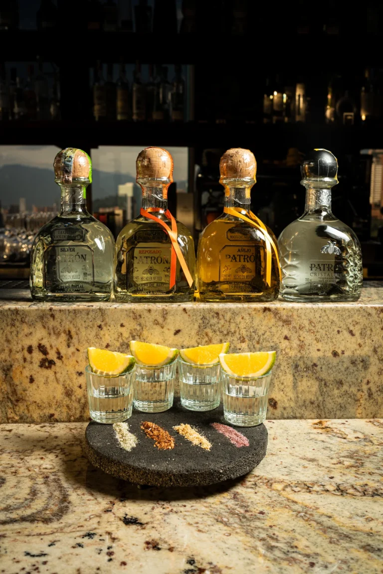 Fotografía gastronómica de cuatro botellas Patrón con shots y sales artesanales sobre barra de mármol — Jose Fonseca Medellín